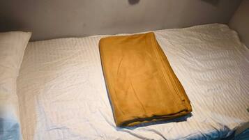 Una cama individual con sábana blanca y manta marrón doblada.