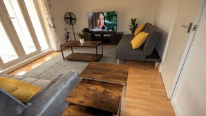 Ein Wohnzimmer mit grauem Sofa, einem Holztisch und einem Fernseher auf einem Holzschrank.