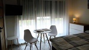 Habitación de hotel con cama, una mesita pequeña con dos sillas, televisor montado en la pared y una lámpara de noche.
