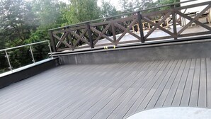 Una terraza de madera con barandilla, rodeada de árboles.