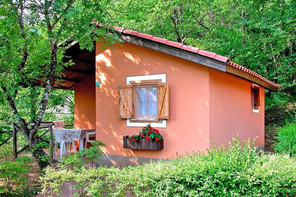 A small, single-story building with a red roof, a window with wooden shutters, and a flower box with red flowers.