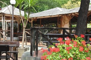 A rustic outdoor seating area with wooden tables and chairs, surrounded by greenery and a thatched-roof structure. - Holiday Village Caravelle Camping Vill, Ceriale (Ceriale)