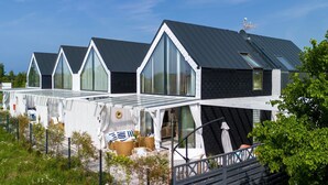 A row of modern, triangular-roofed cabins with large windows, a covered outdoor seating area, and a fenced garden. - Comfortable House With, Whirlpool Bathtub Wrzosowo (Kamien Pomorski)