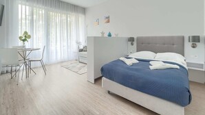 A modern bedroom with a large bed, a small table with chairs, and a sofa. - Apartment in Pobierowo Near Baltic Beach (Rewal)