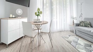 A modern living room with a wooden dining table, white chairs, a grey sofa, and a TV mounted on the wall. - Apartment in Pobierowo Near Baltic Beach (Rewal)