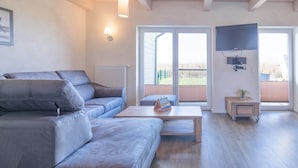 Ein modernes Wohnzimmer mit einem grauen Sofa, einem Holztisch und einem an der Wand befestigten Fernseher.