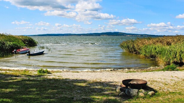 Un lago calmo con barche, una spiaggia sabbiosa e un cielo sereno.
