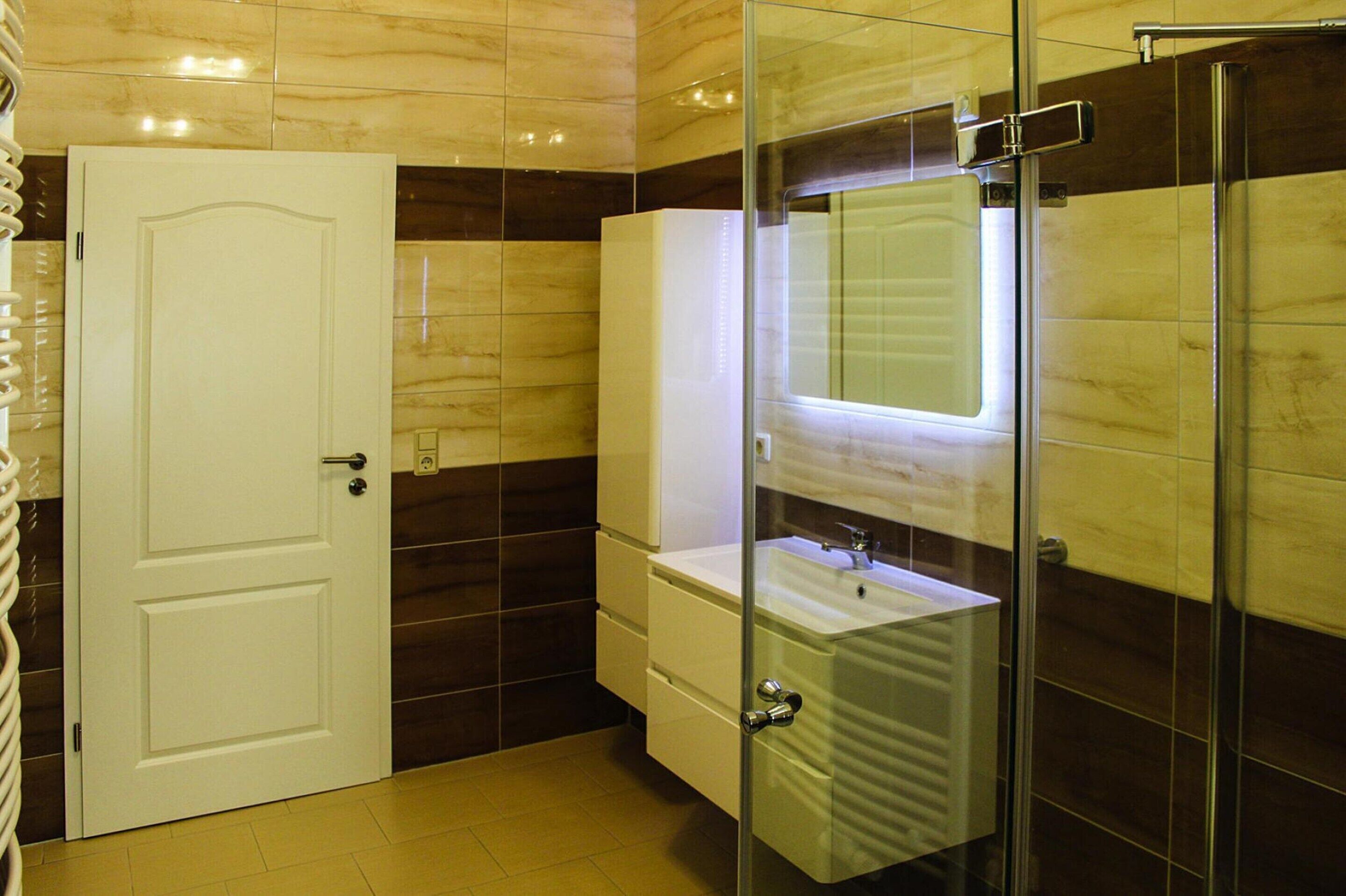 A bathroom with a glass shower enclosure, a white sink, and a door.