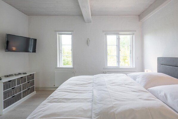 Quarto com cama, televisão fixada na parede e duas janelas.