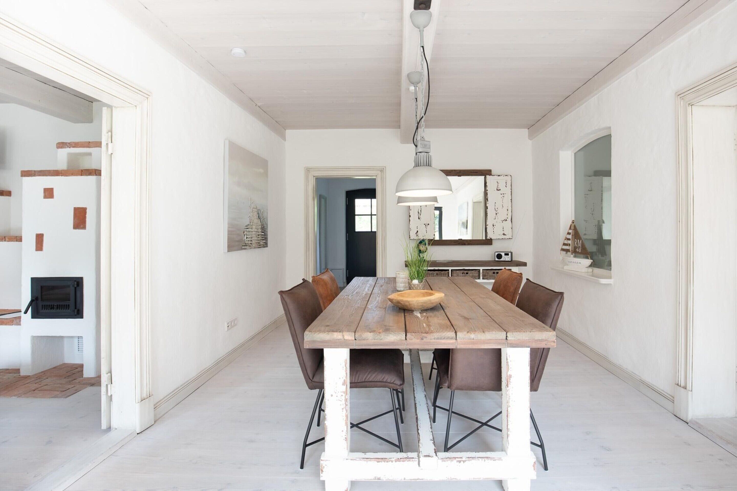 Un coin repas avec une table en bois rustique, six chaises, un luminaire suspendu et un plafond blanc.