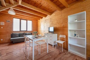 Una cabaña acogedora con interior de madera, un comedor con mesa y sillas, un sofá, un televisor y una estantería.