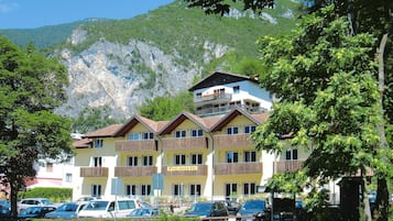Ein mehrstöckiges Hotel mit Balkonen, einem Parkplatz und einer Bergkulisse.