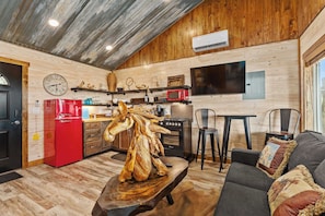 A rustic kitchen with wooden walls, a red refrigerator, a wooden sculpture centerpiece, and a dining area with a table and chairs. - Rockin' R - Shooting Star Cabin (Fredericksburg)