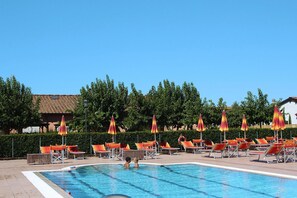 A swimming pool with lounge chairs and umbrellas, surrounded by trees and buildings. - Apartment in Vada With Garden Furniture (Rosignano Marittimo)