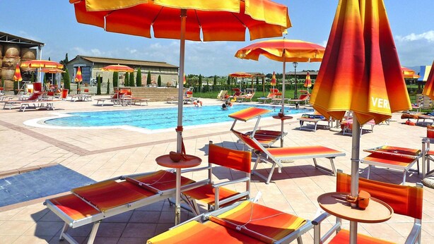 Ein Poolbereich mit mehreren Liegestühlen und Sonnenschirmen, einem Schwimmbecken und einem Gebäude im Hintergrund.