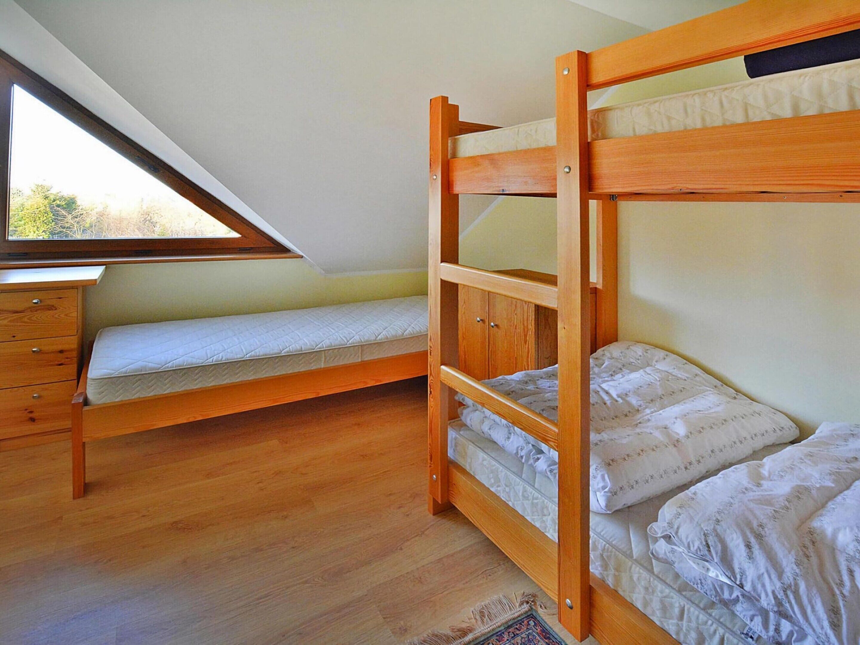 A bunk bed room with a wooden desk and drawers, a slanted ceiling window, and a patterned rug.