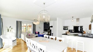 A modern kitchen with white cabinetry, a central island, and a dining area with a white table and chairs. - Ferienwohnung in Wyk auf Foehr (Wyk auf Foehr)