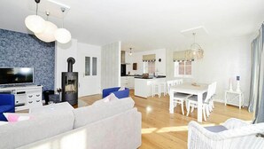 A modern living room with a sofa, TV, and fireplace. There is a dining area with a table and chairs. - Ferienwohnung in Wyk auf Foehr (Wyk auf Foehr)