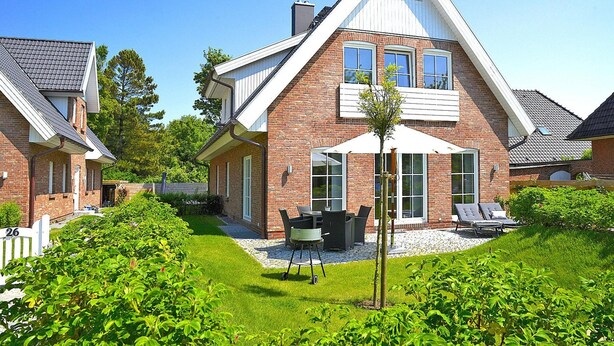 A two-story house with a brick exterior, a covered patio with a table and chairs, and a small garden area. - Ferienwohnung in Wyk auf Foehr (Wyk auf Foehr)