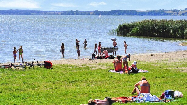 A lakeside scene with people relaxing on the grass and in the water. - Ferienhauser am Kummerower See, Verchen (Verchen)