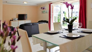 A dining area with a glass table, chairs, and a vase with flowers. There is a sofa and a television in the background. - Ferienhauser am Kummerower See, Verchen (Verchen)
