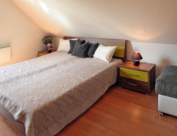 A bedroom with a bed, bedside tables, a lamp, a potted plant, and a small ottoman.