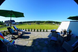 A patio with outdoor seating, a view of a grassy field, and a house in the background. - Comfortable and Spacious Holiday Home, Mielenko (Mielno)