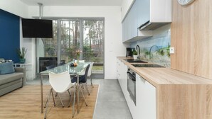 A modern kitchen with a glass dining table, white cabinets, and a wooden countertop. - Comfortable Apartment Close to a Sandy Beach (Rewal)