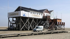 Ein Gebäude am Strand mit einer Holzterrasse und einem davor geparkten Wagen.