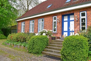 A red brick house with a blue door and windows, a small garden with hedges, and a cobblestone path leading to the entrance. - Ferienwohnung im Gutshaus Schulenbrook (Metelsdorf)