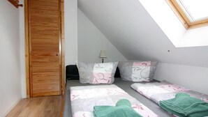 A small, well-lit room with a sloped ceiling, a wooden door, and two beds with floral bedding and green towels. - Ferienwohnung im Gutshaus Schulenbrook (Metelsdorf)
