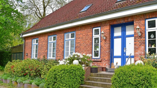 A traditional brick house with a blue door, white-framed windows, and a small garden with hedges and flowers. - Ferienwohnung im Gutshaus Schulenbrook (Metelsdorf)
