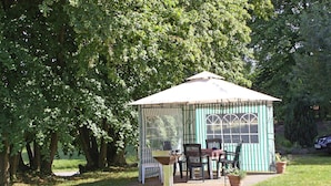 A gazebo with a green and white striped exterior, a table with chairs, and potted plants. - Ferienwohnung im Gutshaus Schulenbrook (Metelsdorf)