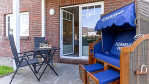 Un patio con una mesa y sillas, un sofá de mimbre con un cojín azul y un edificio de ladrillo con una puerta corredera de vidrio.