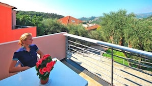 Un balcón con barandilla, una mesa con planta en maceta y vistas a un paisaje montañoso.