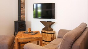 A living room with a sofa, a wooden coffee table, a TV mounted on the wall, and a wood-burning stove. - Ferienwohnung, Zemitz (Zemitz)