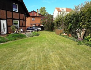 A residential property with a well-maintained lawn, a patio area with outdoor furniture, and a garage with two cars parked inside. - Ferienwohnung in der Huebschen Inselstadt Malchow (Malchow)