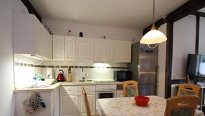 Una cucina compatta con mobili bianchi, un forno a microonde, un frigorifero e un tavolo con sedie.