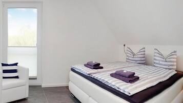 Ein modernes Schlafzimmer mit Bett, Sessel und großem Fenster.