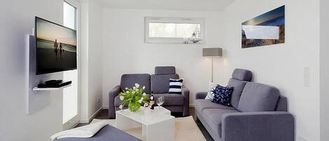 A modern living room with a flat-screen TV, grey sofas, a coffee table with a vase, and a painting on the wall.