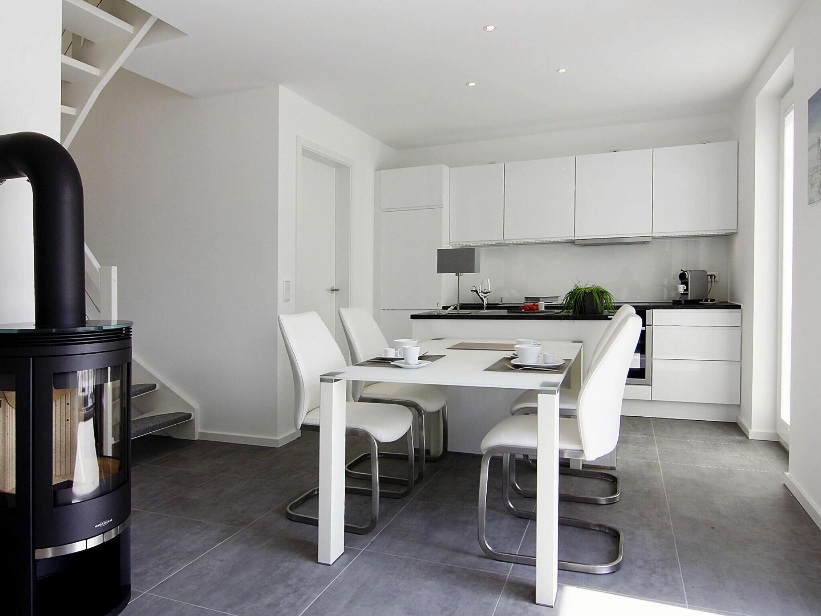 A modern kitchen with white cabinets, a dining table with chairs, and a black stove.