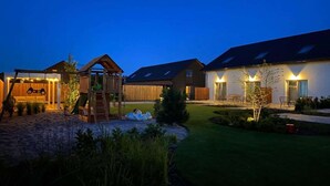 Una propiedad residencial con una zona de juegos de madera, un espacio de estar cubierto y un patio bien iluminado.