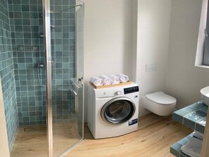 A compact bathroom with a glass shower enclosure, a front-loading washing machine, a toilet, and a small sink area. - Holiday Home in Grzybowo Near Wide Beach (Kołobrzeg)