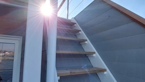 Una escalera de madera con peldaños que conducen a una plataforma, junto a una puerta blanca.