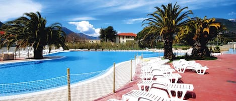 A pool area with lounge chairs and palm trees, surrounded by buildings and mountains.