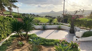 Jardim ajardinado com um muro branco curvo, diversas plantas e vista para colinas ao longe.