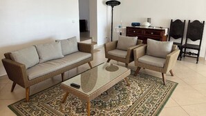 Sala de estar com sofá, duas poltronas, mesa de centro, abajur e tapete estampado.