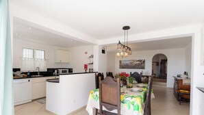 Cozinha espaçosa com área de refeições, incluindo uma ilha central, cadeiras de madeira e um lustre.