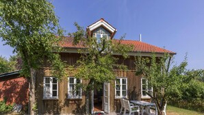 Une maison en bois avec un toit recouvert de tuiles rouges, une partie en briques sur le côté gauche et une terrasse avec des meubles d’extérieur.