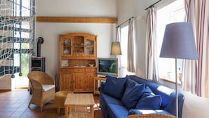 Un salon avec un canapé bleu, des fauteuils en osier, un meuble en bois, une télévision et une lampe.